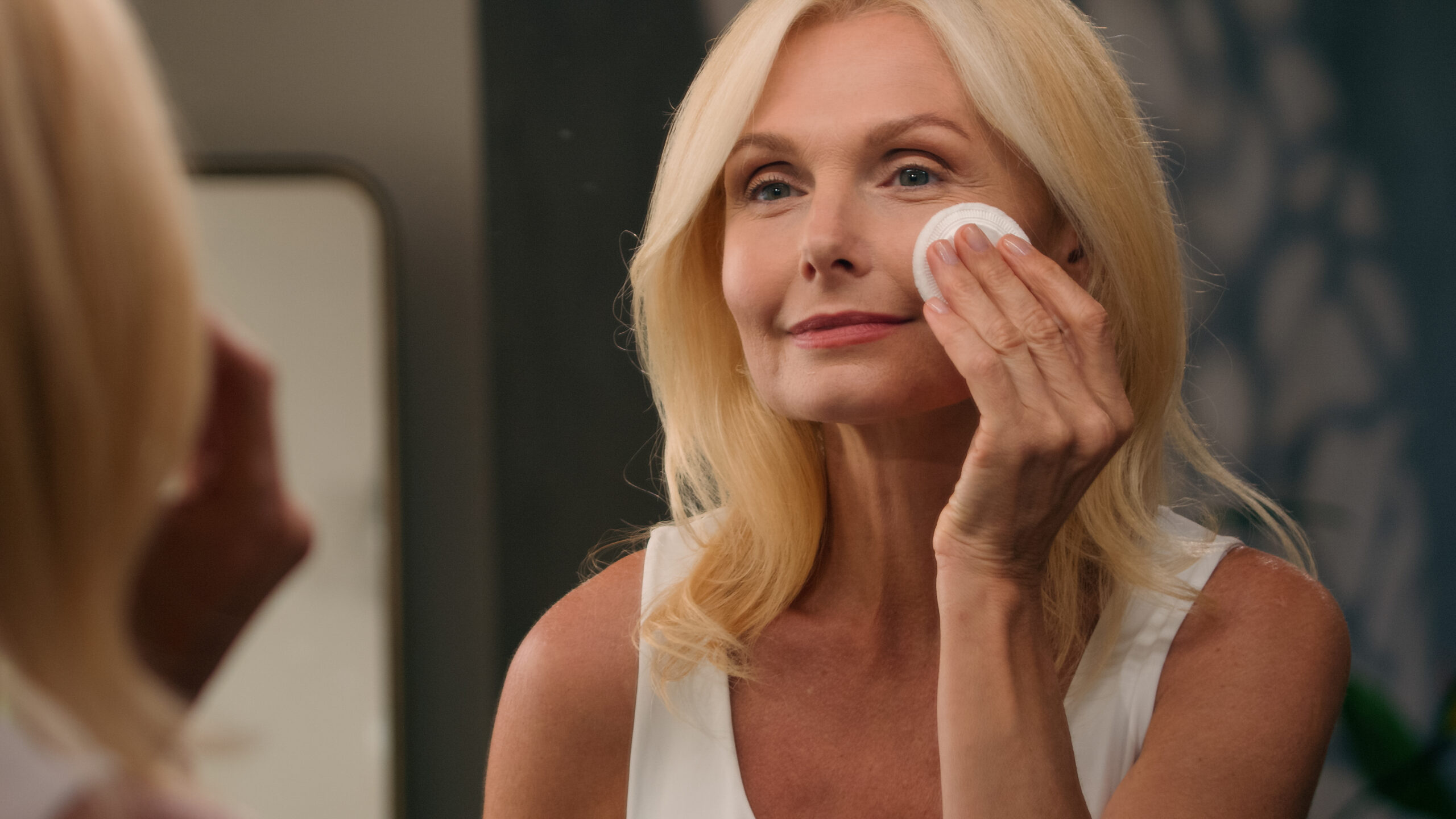 Beautiful middle-aged 50s old lady mature woman applying powder luxury cosmetics on face with cotton pad perfect smooth skin natural makeup in mirror home bathroom facial wrinkles anti-aging beauty How Age Affects Brow Lift Needs